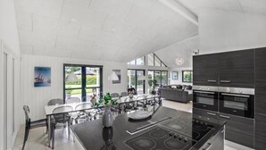 Cozinha moderna com ilha central, área de refeições com cadeiras e vista para o exterior.