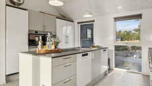 A modern kitchen with white cabinetry, a central island with a wooden countertop, and a built-in dishwasher. - VillaVilla 653 - Vejers, Vestjylland (Vejers Strand)