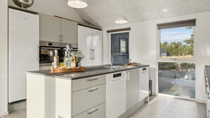 A modern kitchen with white cabinetry, a central island with a wooden countertop, and a built-in dishwasher. - VillaVilla 653 - Vejers, Vestjylland (Vejers Strand)
