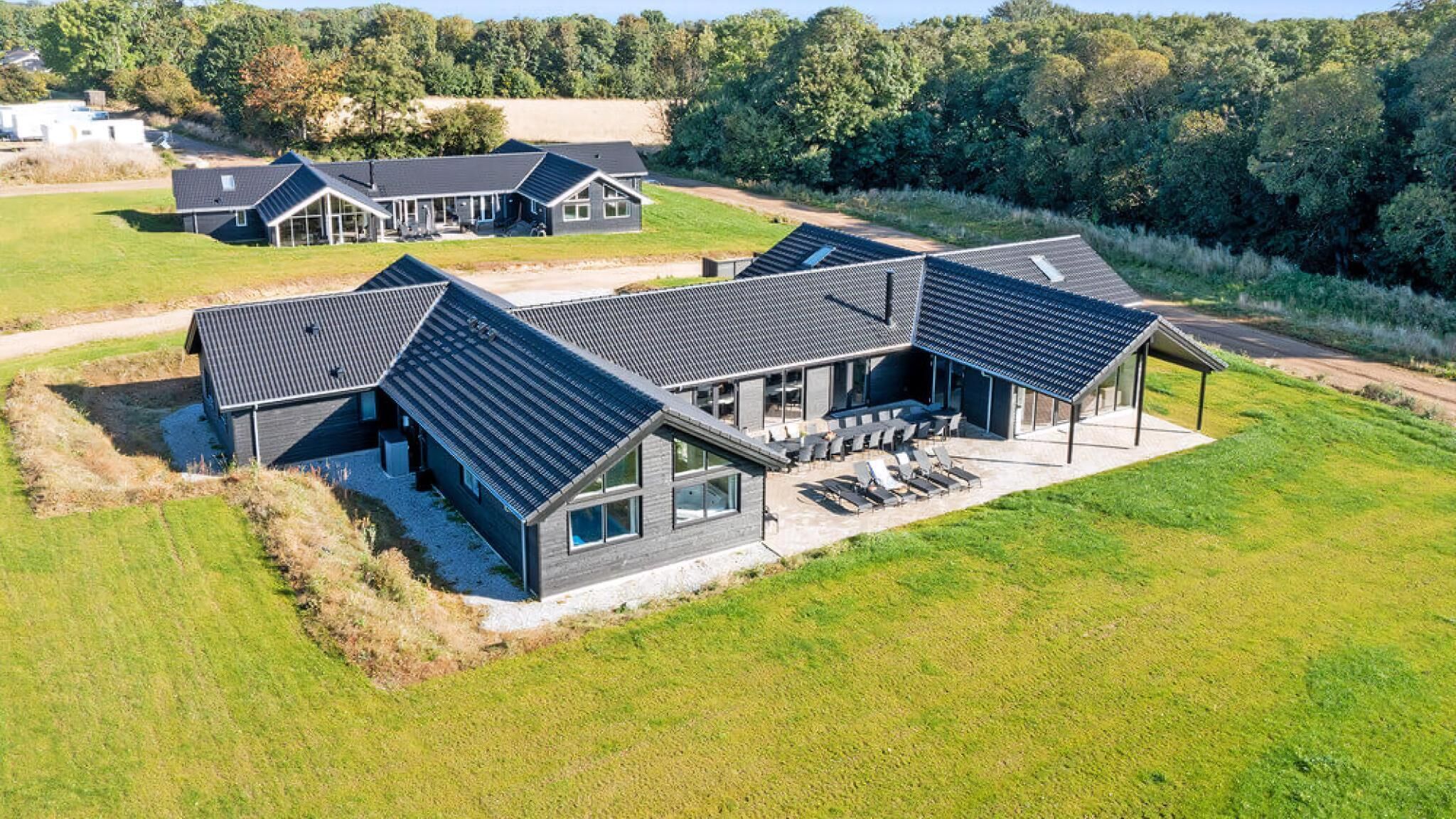 A modern house with a large patio area, multiple rooms, and a surrounding grassy landscape.