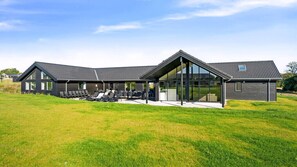 Un edifici modern amb una gran façana de vidre, zona d'seients exteriors i un teulat inclinat.