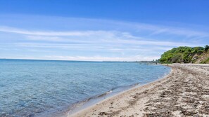 Une plage à l’eau claire, une rive sablonneuse et une colline boisée.