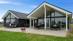 Ein modernes Haus mit überdachter Terrasse, großen Fenstern und schwarzem Anstrich.