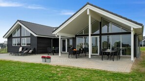 Une maison moderne dotée d’un patio couvert, de grandes fenêtres et d’une façade noire.