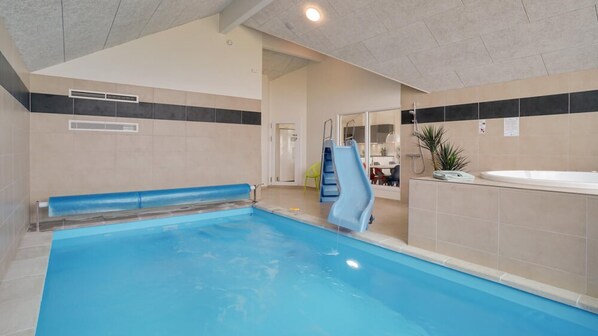 An indoor swimming pool with a slide, a shower area, and a seating area with a bench.