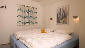 Une chambre à coucher avec un lit, un ours en peluche, un tableau et un luminaire fixé au mur.