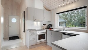 A modern kitchen with white cabinetry, a built-in oven, a coffee maker, and a window with a view of trees. - VillaVilla 578 - Marielyst, Lolland/Falster/møn (Idestrup)
