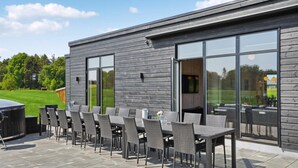 Un patio al aire libre con una mesa larga y sillas, una parrilla y una terraza de madera.
