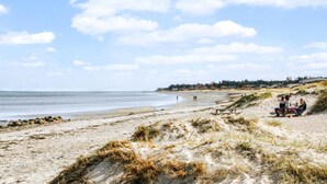 Una playa arenosa con dunas, una mesa de picnic y algunas personas.