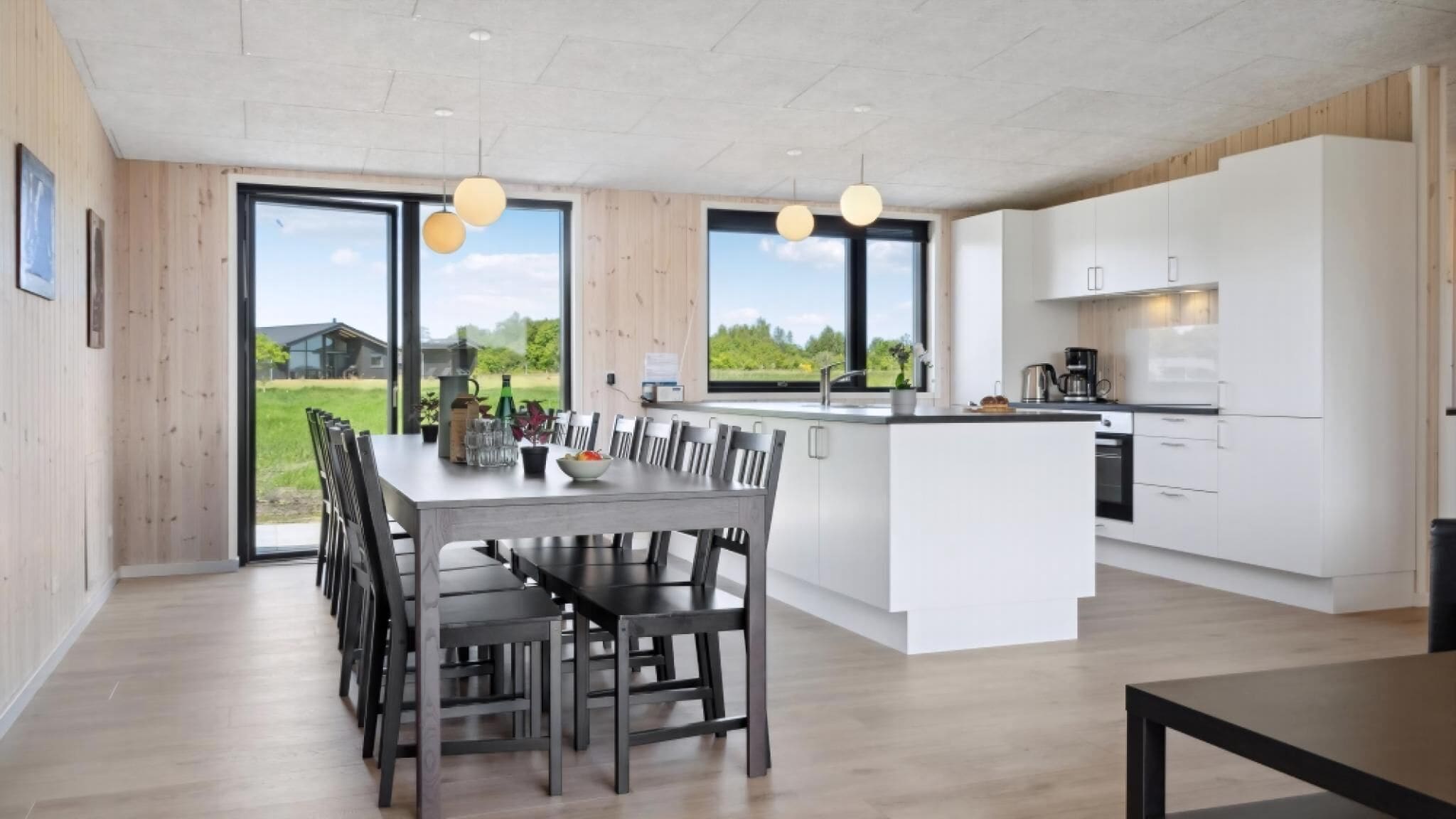 Una cocina moderna con armarios blancos, una isla central y una zona de comedor con mesa y sillas.