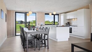 Una cocina moderna con armarios blancos, una isla central y una zona de comedor con mesa y sillas.