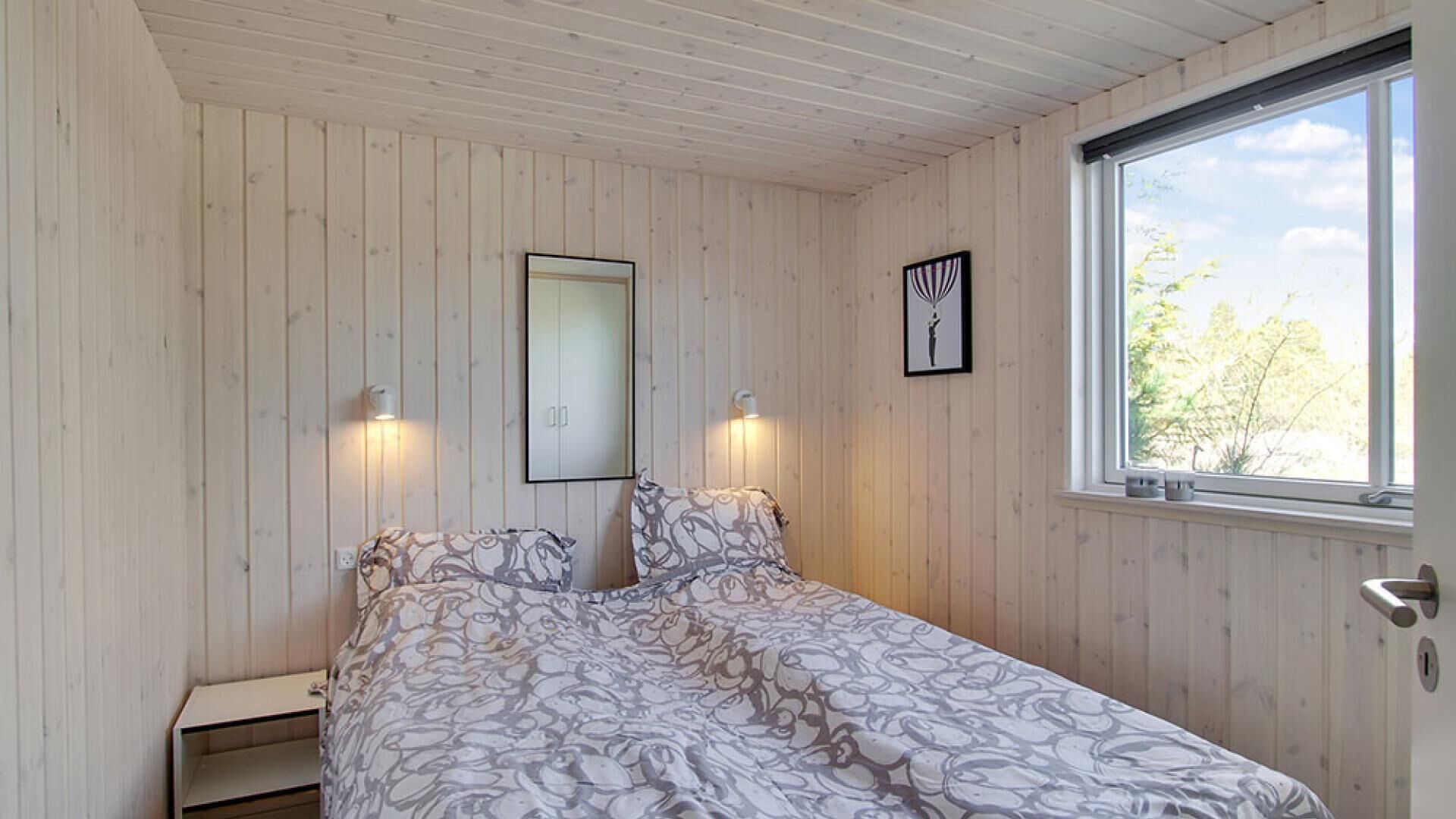 A bedroom with a bed, two wall-mounted lights, a window, and a door.