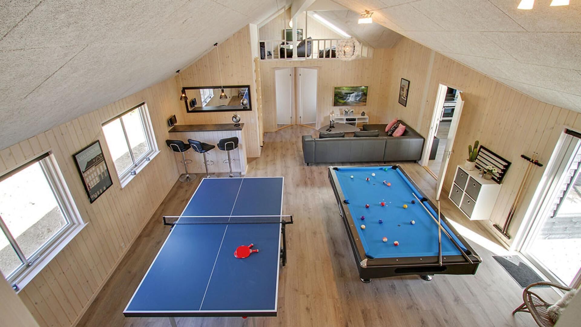Ett rymligt rum med ett bordtennisbord, ett biljardbord och en sittgrupp med en soffa och stolar.
