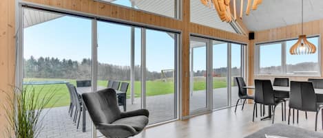 A spacious room with large sliding glass doors leading to an outdoor patio, a dining area with black chairs, and a modern pendant light.