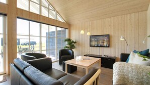 A modern living room with a wooden ceiling, large windows, a black leather sofa, a wooden coffee table, and a TV mounted on the wall. - VillaVilla 302 - Saksild, Østjylland (Odder)