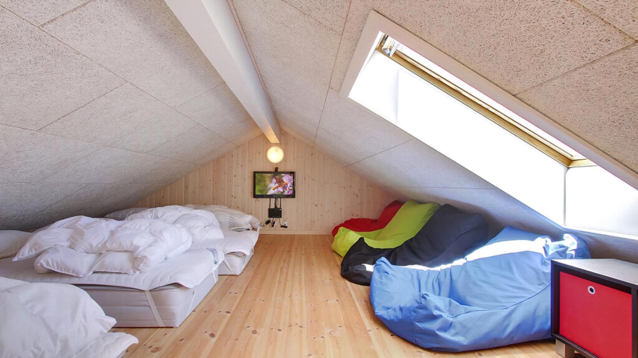 A small attic bedroom with two beds, a TV, and a slanted ceiling.