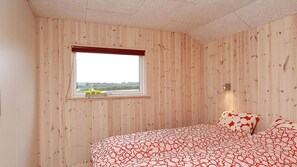 A bedroom with wooden paneling, a window with a view, and a bed with patterned bedding.
