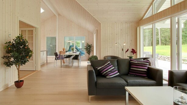 Un interior moderno con piso de madera, un sofá con cojines a rayas, un comedor con mesa y sillas, y ventanas amplias que ofrecen vistas al exterior.