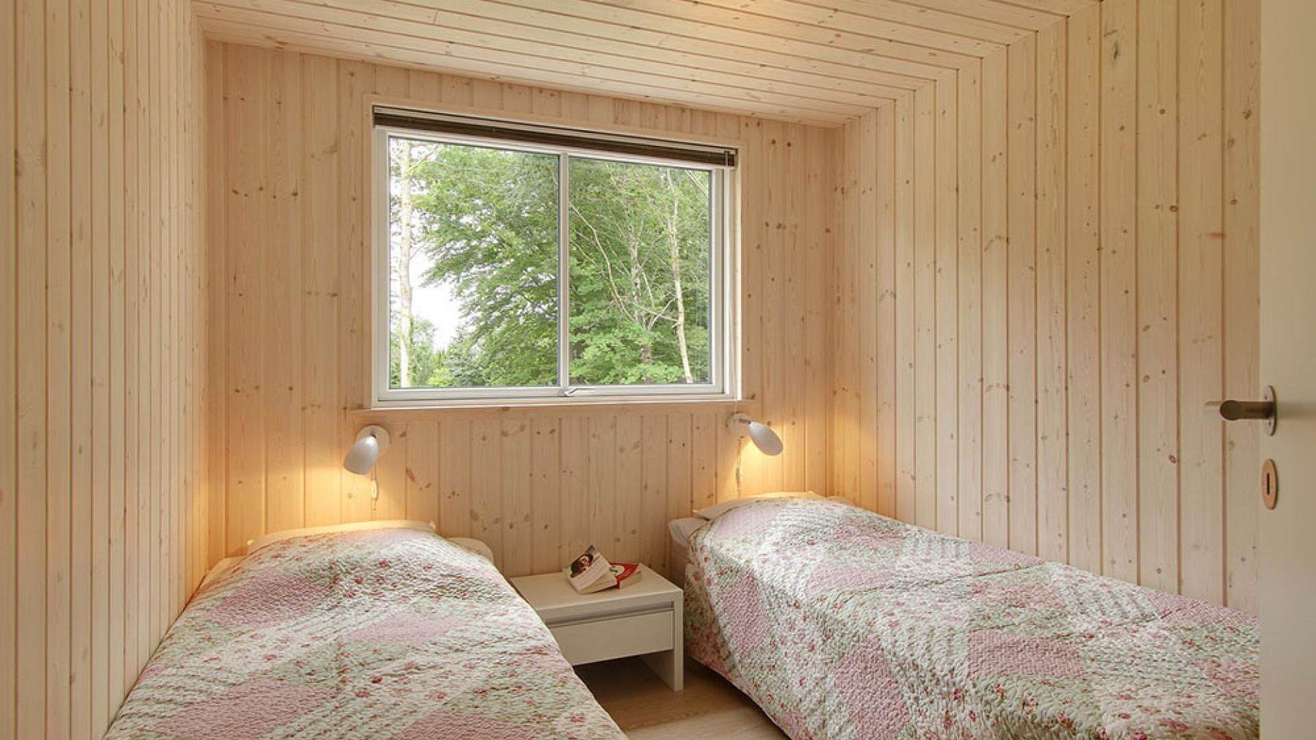 A room with two beds, a window, and a nightstand with a book.