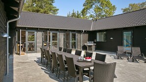 Un patio al aire libre con una larga mesa de comedor y sillas, una parrilla y una vista de una piscina y un tobogán al fondo.