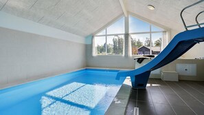 Una piscina interior con un tobogán azul, ventanas amplias y vistas al exterior.