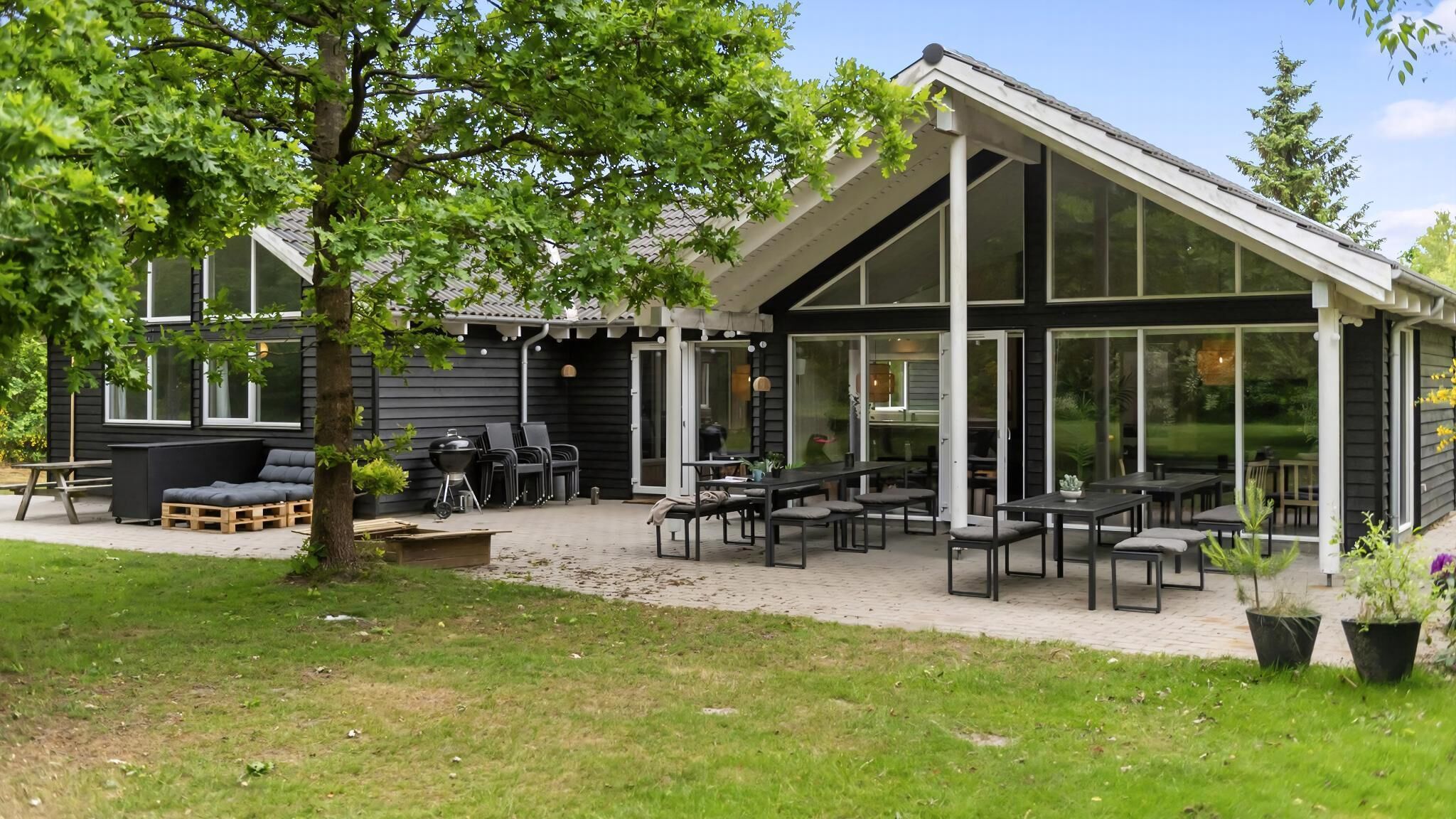 Ein moderner Außenbereich mit Tischen, Stühlen, einem Grill und einer überdachten Terrasse.