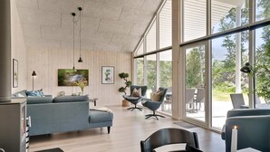Uma sala de estar moderna com sofá, cadeiras, televisão e janelas amplas.