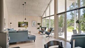 Een moderne woonkamer met een bank, stoelen, een televisie en grote ramen.