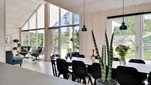 Uma área de refeições moderna com janelas amplas, cadeiras pretas e uma mesa com um vaso de flores.