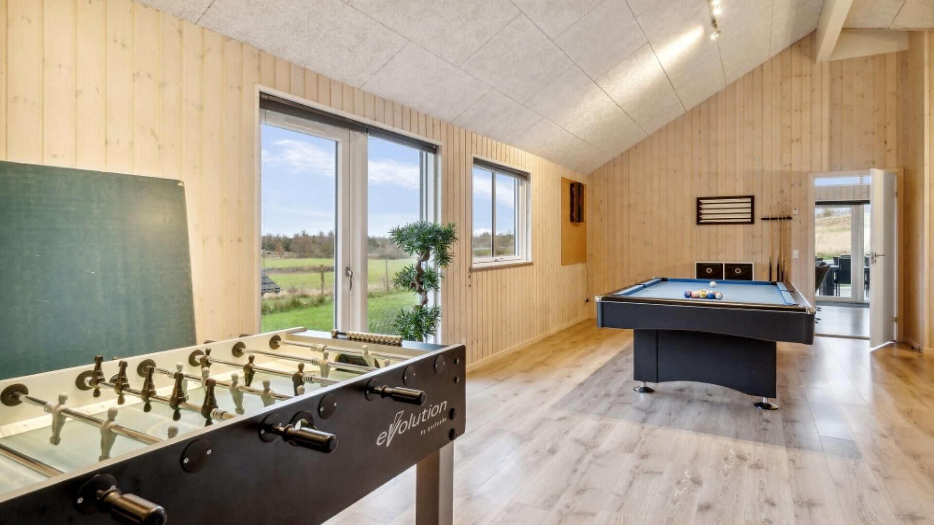 Una habitación con mesa de fútbol de mesa y mesa de billar, paredes de madera, ventanas grandes y vistas al exterior.