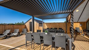 Ein Terrassenbereich im Freien mit überdachter Sitzgelegenheit, einem Esstisch und Lounge-Stühlen.