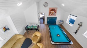 Ein Billardtisch mit Billardkugeln, ein Kicker und zwei Sofas in einem Raum mit weißen Wänden und Holzböden.