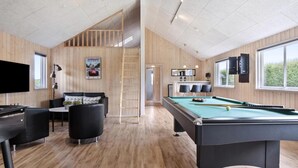 Een pooltafel, een televisie, een bank en een houten wand met een poster.