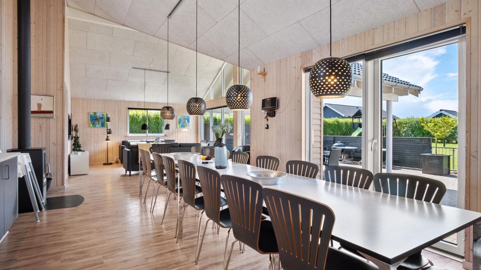 A modern dining area with a long table and chairs, large windows, and pendant lighting.