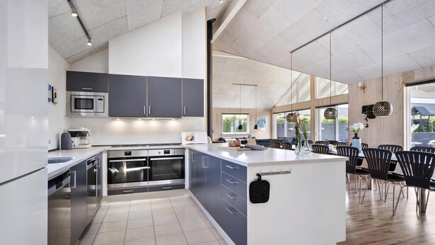 Een moderne keuken met inbouwapparatuur, een groot kookeiland en een eethoek met stoelen.