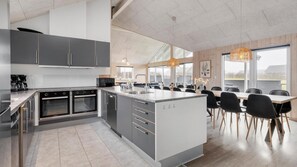 A modern kitchen with built-in appliances, a large island, and a dining area with a view. - VillaVilla 322 - Skåstrup Strand, Fyn og øer (Bogense)