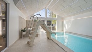 A modern indoor swimming pool with a glass wall, a slide, and a potted plant. - VillaVilla 273 - Blåvand, Vestjylland (Blåvand)
