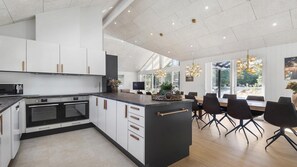 A modern kitchen with white cabinetry, a central island, and a dining area with a large window. - VillaVilla 273 - Blåvand, Vestjylland (Blåvand)