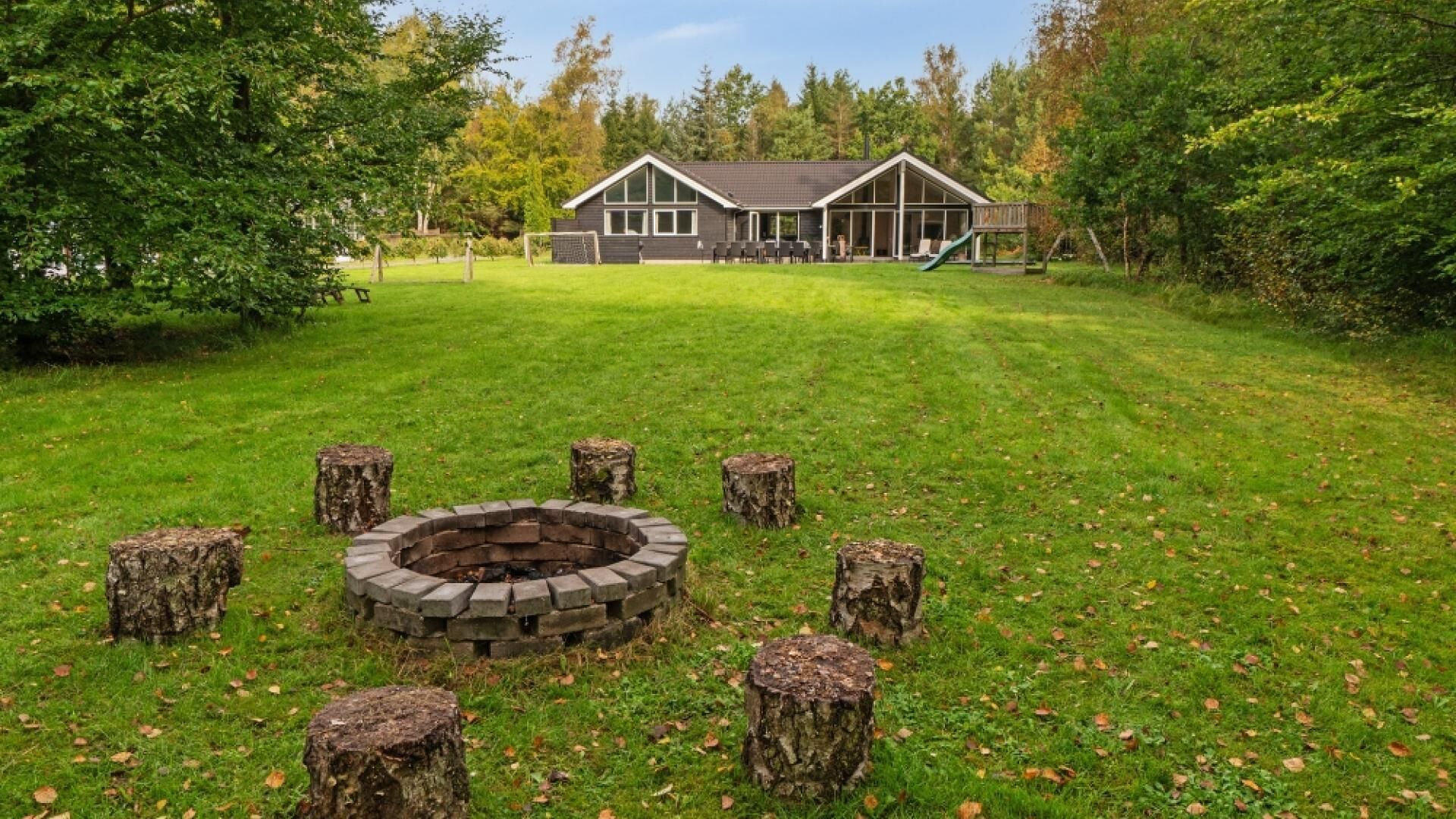 A house with a large deck and a fire pit surrounded by tree stumps.