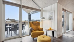 Un interno moderno con un'ampia porta scorrevole in vetro che dà su uno spazio esterno, una poltrona comoda, un piccolo tavolino e un quadro appeso al muro.