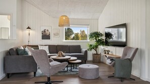Ein modernes Wohnzimmer mit einem grauen Sofa, zwei Sesseln, einem Couchtisch und einem an der Wand montierten Fernseher.