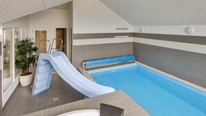 Ein Hallenbad mit Rutsche, einer Topfpflanze und einem Duschbereich.