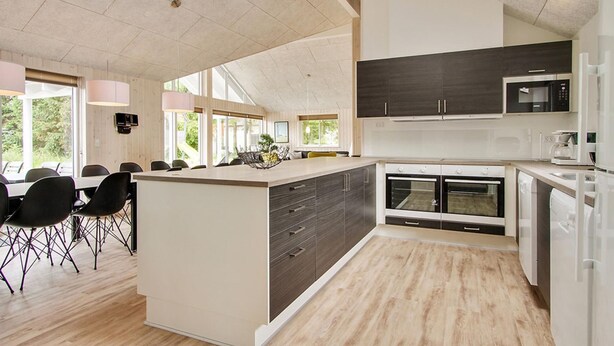 A modern kitchen with a large island, built-in ovens, and a dining area with chairs. - VillaVilla 355 - Lohals, Fyn og øer (Tranekær)