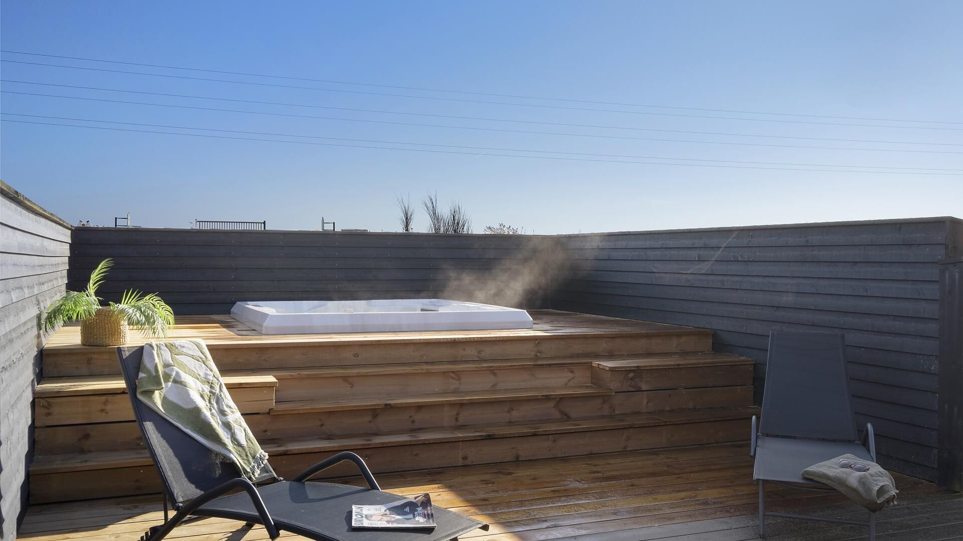 Eine Dachterrasse mit Whirlpool, Holzstufen, Liege und Bank.