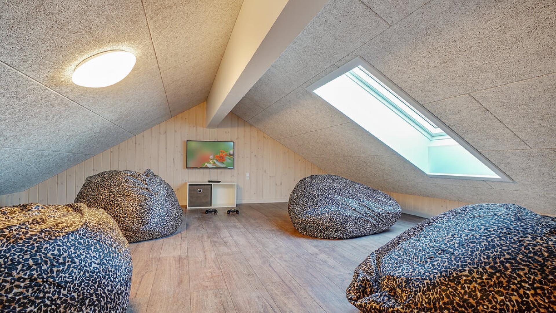 Ein modernes Dachzimmer mit schrägen Wänden, einem Oberlicht und einer gemütlichen Sitzecke mit großen, gemusterten Sitzsäcken.