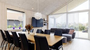 Un comedor moderno con mesa de madera y sillas negras, un sofá, y un ventanal con vistas al exterior.