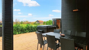 A wooden deck with outdoor furniture, a hot tub, and a view of a green field and houses. - VillaVilla 650 - Marielyst, Lolland/Falster/møn (Væggerløse)