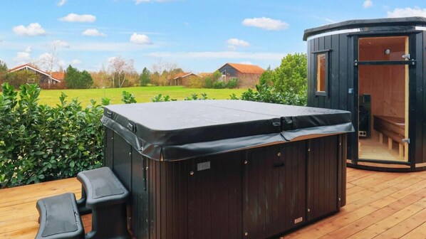 Un jacuzzi con terraza de madera y un banco de madera, rodeado de follaje.