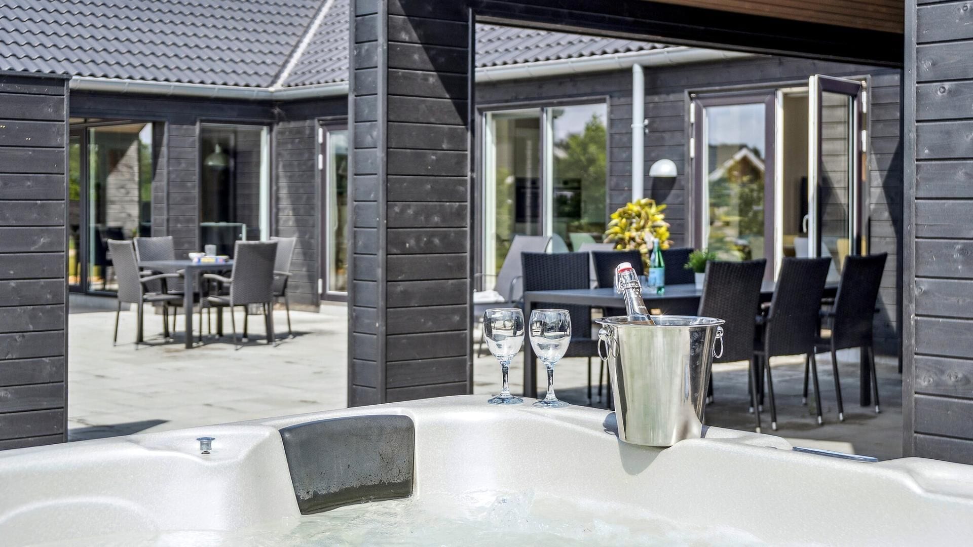 Ein moderner Außenbereich mit Sitzgelegenheit, Whirlpool, zwei Gläsern und einer Champagnerflasche.