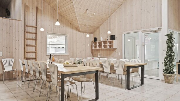 Una stanza spaziosa con pareti in legno, un'ampia finestra e un ingresso che conduce al bagno. Sono presenti diversi tavoli e sedie disposti per la sala da pranzo.